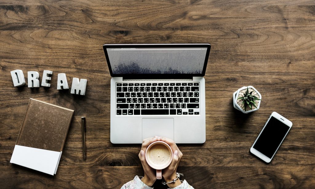 Busy desk with a pair of hands holding a coffee mug