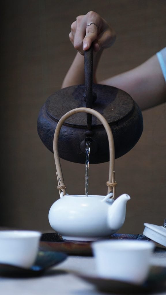 person pouring water on ceramic teapot