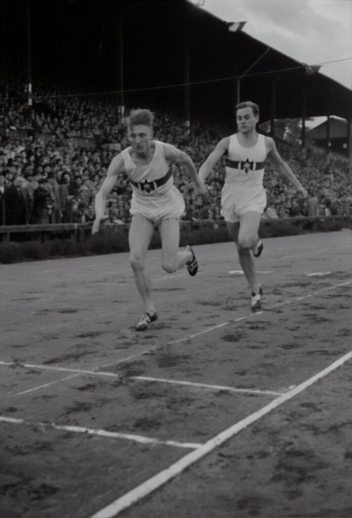 grayscale photography of men racing on track and field surrounded with people watching them