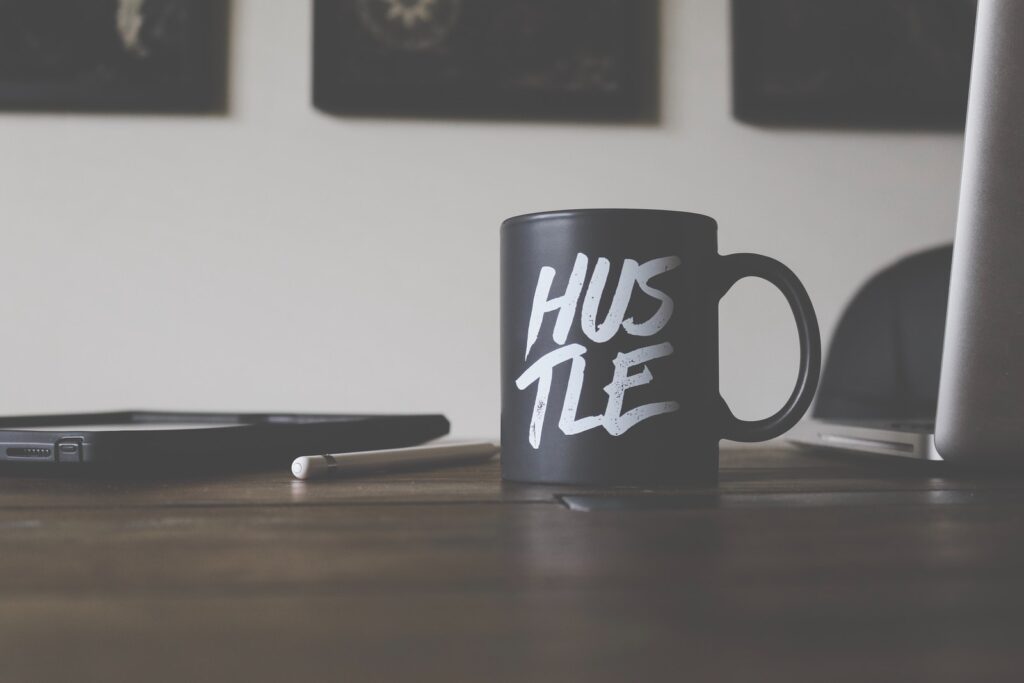 black and white Hustle-printed ceramic mug on table. Hustling is very Wood!